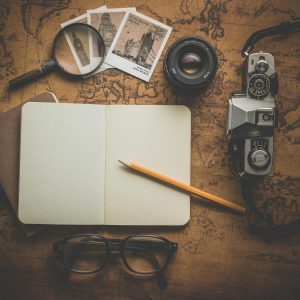 A Flat Lay Of Travel Essentials On A Vintage Map Surface, Including A Camera, Notebook, And Magnifying Glass.