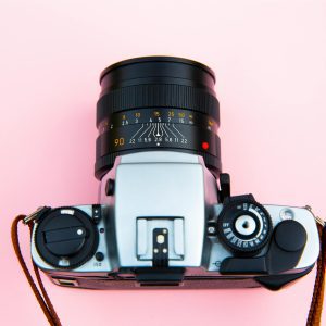A Classic Analog Camera With A Lens On A Vibrant Pink Background.