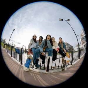 Group Of Young Women Sitting By A Railing, Enjoying A Sunny Day Together.