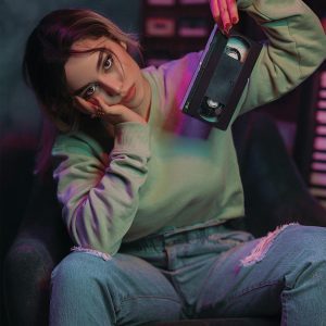 Young Woman In Vibrant Colors Posing With A VHS Tape, Evoking 90s Nostalgia.