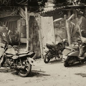 Three Parked Motorcycles And Scooters In A Rustic Urban Setting, Captured In Monochrome.