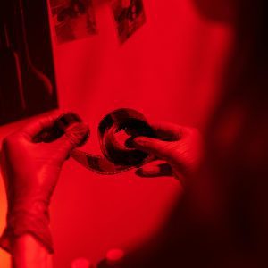 A Person Examining Film Negatives In A Darkroom Under Red Light.