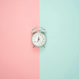 A Vintage Round Clock On A Split Pastel Pink And Blue Background.
