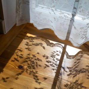 Lace Curtains Casting Delicate Floral Shadows On A Hardwood Floor In Warm Sunlight, Creating A Vintage Ambiance.