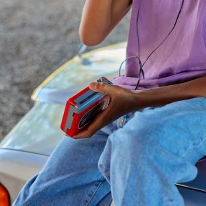 Teenager Enjoying Music On A Red Retro Walkman, Sitting On A Car Hood.