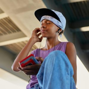 Teenager With Headphones And Vintage Walkman Sitting Outdoors, Enjoying Music Under A Bridge.
