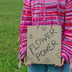 Person Holding A 'Flower Power' Sign, Symbolizing Peace And Activism In A Vibrant Setting.