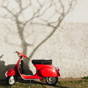 A Vibrant Red Vintage Scooter Parked Against A Textured Wall In Porto, Portugal.