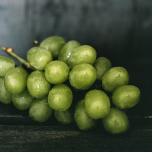 Cluster Of Fresh Green Grapes With Droplets On Dark Wooden Surface, Highlighting Freshness.