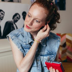 Caucasian Woman In Denim Vest Listens To A Cassette Player Indoors, Capturing Vintage Nostalgia.