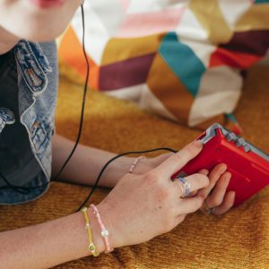 Young Person Relaxing Indoors, Listening To Music With A Red Vintage Walkman And Earphones.