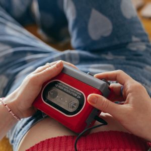 Close Up Of Hands Holding A Red Cassette Player, Wearing Heart Pattern Jeans, Embodying A Retro Aesthetic.