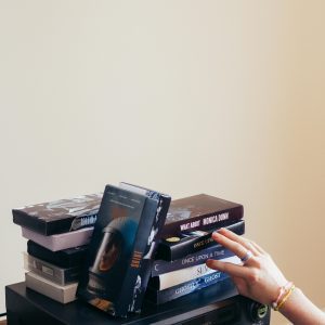 A Hand Reaches For A VHS Tape From A Stack On A Vintage VHS Player, Indoors.