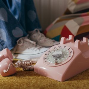 A Nostalgic Pink Rotary Telephone On A Vintage Carpet With Jeans Featuring Heart Patches.