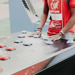 Group Of Young Adults Enjoying Outdoor Arcade Buttons Game In A Park Setting.