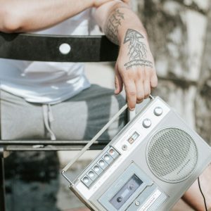 A Tattooed Person Holds A Retro Boombox, Sitting Casually Outdoors, Embracing Nostalgia.