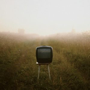 A Lone Vintage TV On A Stool Amidst A Foggy Grass Field, Evoking Nostalgia And Mystery.