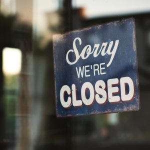 A Vintage "Sorry We're Closed" Sign On A Glass Door Reflects Street View Outside.