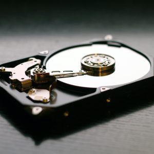 An Open Hard Drive Is Displayed On A Wooden Surface, Showcasing Its Internal Components And Metallic Details.