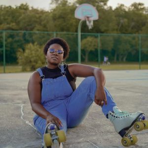A Confident Woman Sitting On A Roller Rink Wearing Roller Skates And Sunglasses.