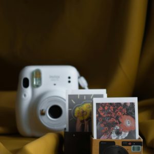 A White Instant Camera Next To Colorful Polaroid Prints On A Yellow Background.