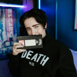 Young Person In Retro Themed Room Holding A VHS Tape, Blending Vintage And Modern Aesthetics.