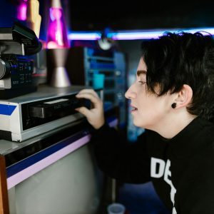 A Person Using A Vintage VHS Player, Surrounded By Retro Decor And Neon Lighting.