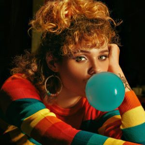 Woman With Colorful 80s Style Blowing Bubble Gum Indoors, Wearing Striped Sweatshirt.