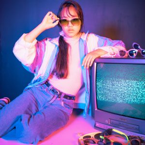 Stylish Model In Sunglasses Poses With Vintage CRT TV, Embracing The Retro 80s Neon Vibe.
