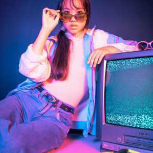 Stylish Asian Woman Posing With Vintage CRT TV, Highlighting 80s Retro Fashion And Neon Colors.