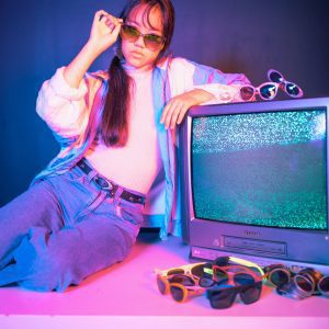 A Stylish Asian Woman Posing In A Retro Setting With CRT TV And Neon Colors.