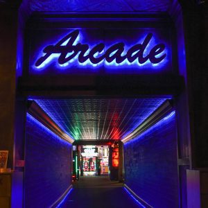 Vibrant Neon Light Hallway Leading To Retro Arcade Gameplay Area.