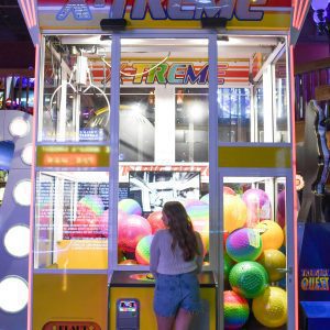 A Young Woman Playing With A Colorful Claw Machine At An Arcade, Filled With Vibrant Balls And Neon Lights.