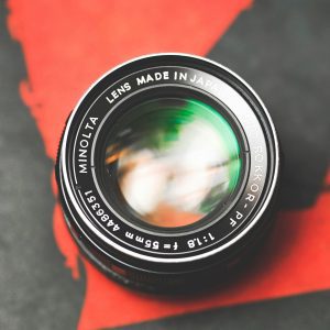Close Up Shot Of A Vintage Minolta Camera Lens On A Red And Black Background.