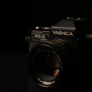 Close Up Image Of A Classic Yashica FX D Film Camera With Lens In A Dark Setting.