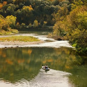 A Kayaker Enjoys A Peaceful Paddle On A Scenic River Surrounded By Vibrant Fall Foliage.