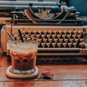 A Cozy Indoor Setting With Iced Coffee And A Vintage Typewriter On A Wooden Table.