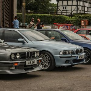 Row Of Classic Cars Parked Outdoors With A Tudor Style House In The Background.