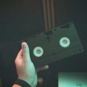 A Hand Holds A Classic VHS Tape, Capturing A Nostalgic Moment In A Dimly Lit Room.