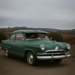 A Vintage Green Car Parked Amidst A Scenic Portland, OR Backdrop, Reflecting Classic Automotive Charm.