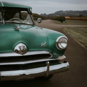 Vintage Green 1950s Car Parked On A Scenic Road, Capturing Retro Elegance.