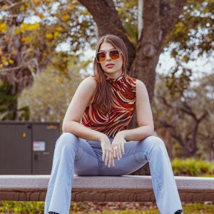Chic Young Woman With Sunglasses Sitting On A Park Bench In Tampa, Exuding A Playful And Relaxed Vibe.