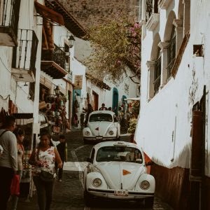 Experience The Vintage Charm Of A Narrow Cobblestone Street In Taxco, Mexico, Lined With Retro Cars And Vibrant Shops.