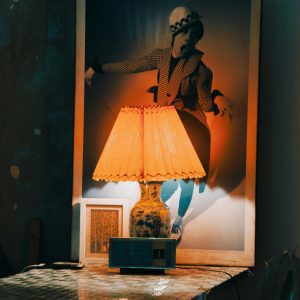 A Warm, Nostalgic Scene Featuring A Lit Lamp Casting Light On A Vintage Poster In A Cozy Room Setting.