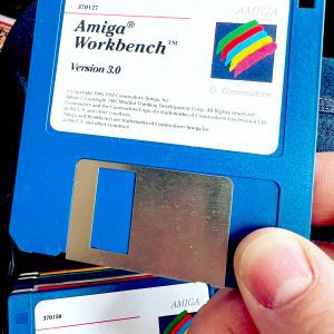 Close Up Of Vintage Amiga Workbench 3.0 Floppy Disk Held By Hand, Showcasing Retro Computing.
