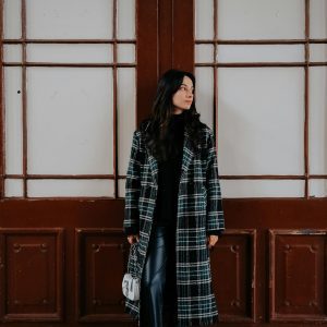 Stylish Woman In A Black And White Checkered Coat Standing Against A Wooden Backdrop.