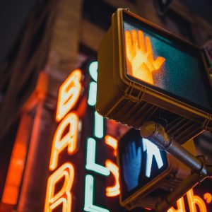 A City Street Scene Featuring A Neon Bar Sign With A Pedestrian Traffic Light At Night.