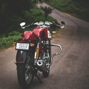 Rear View Of A Classic Red Motorcycle Parked On A Quiet Country Road, Showcasing Vintage Style.