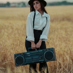 Stylish Woman In Retro Attire Poses With Boom Box In A Wheat Field.