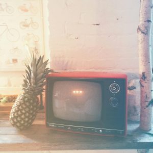 Vintage Red Television With A Pineapple On A Wooden Table Against A Rustic Wall.